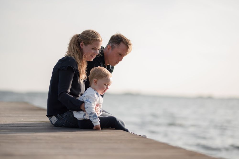 Family sitting together on concrete pier overlooking ocean.