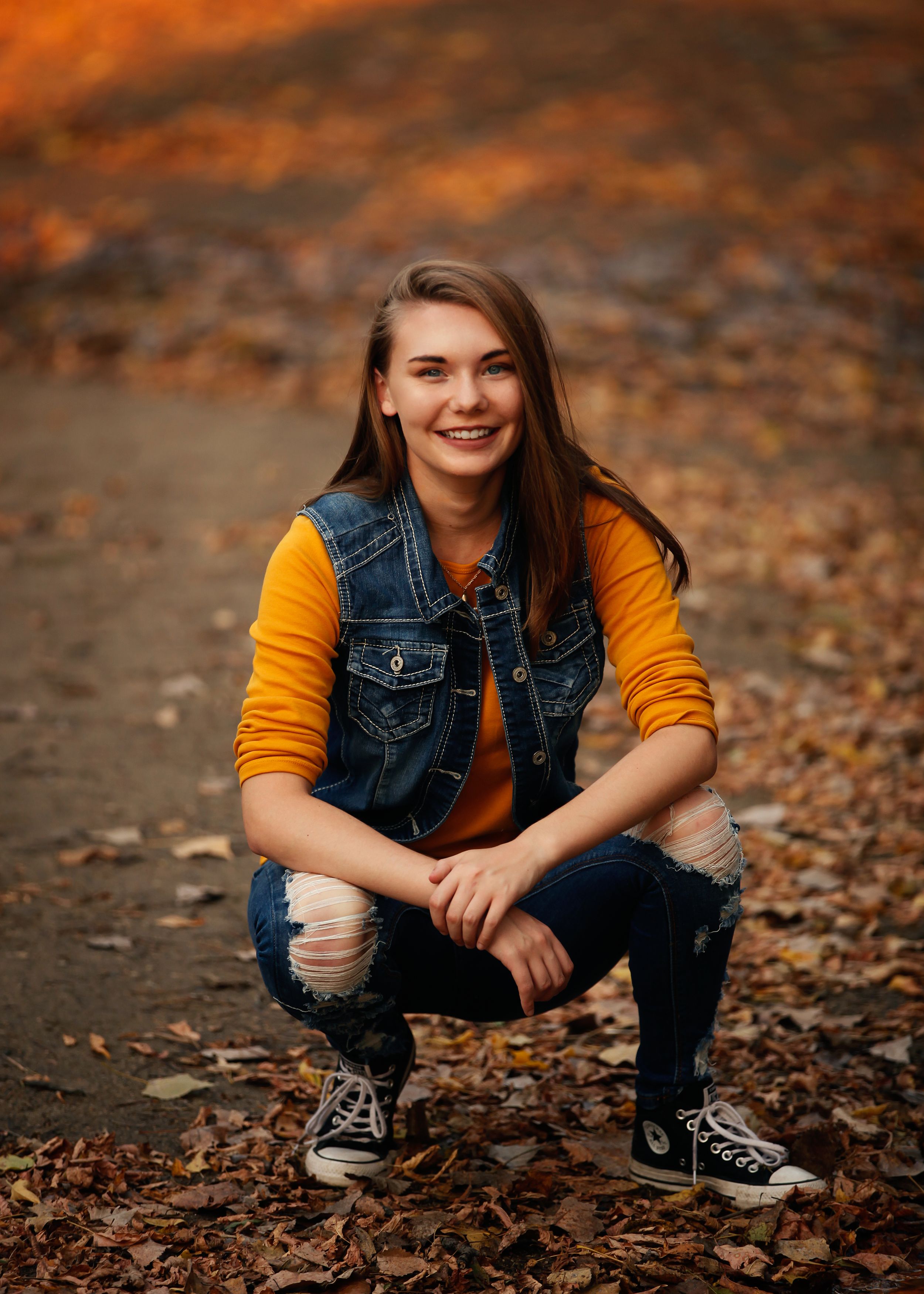 Casual autumn photoshoot featuring denim vest and orange sweater among fallen leaves.