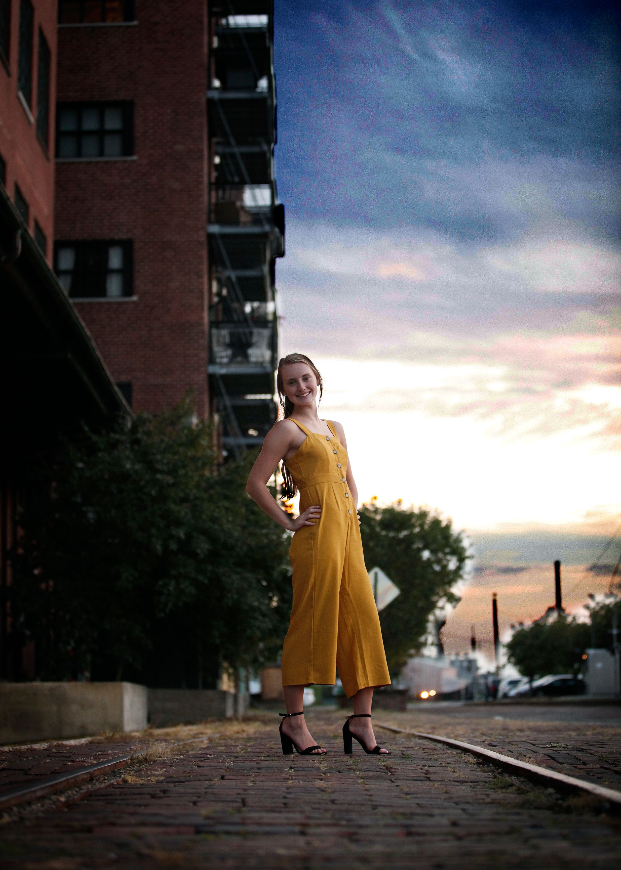 Figure in yellow dress posing on cobblestone street at dusk.