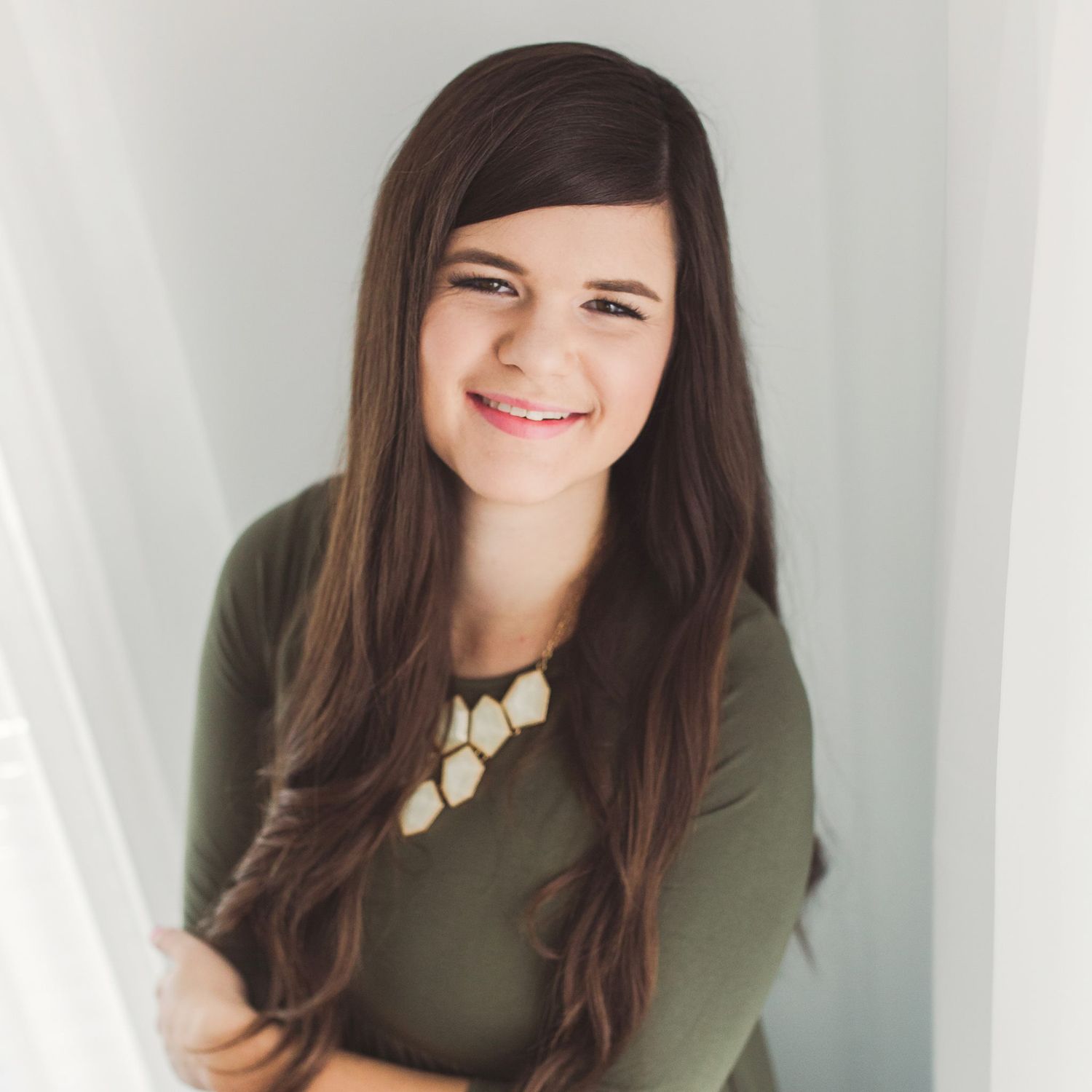 Portrait of someone in olive green top with statement necklace against white background.