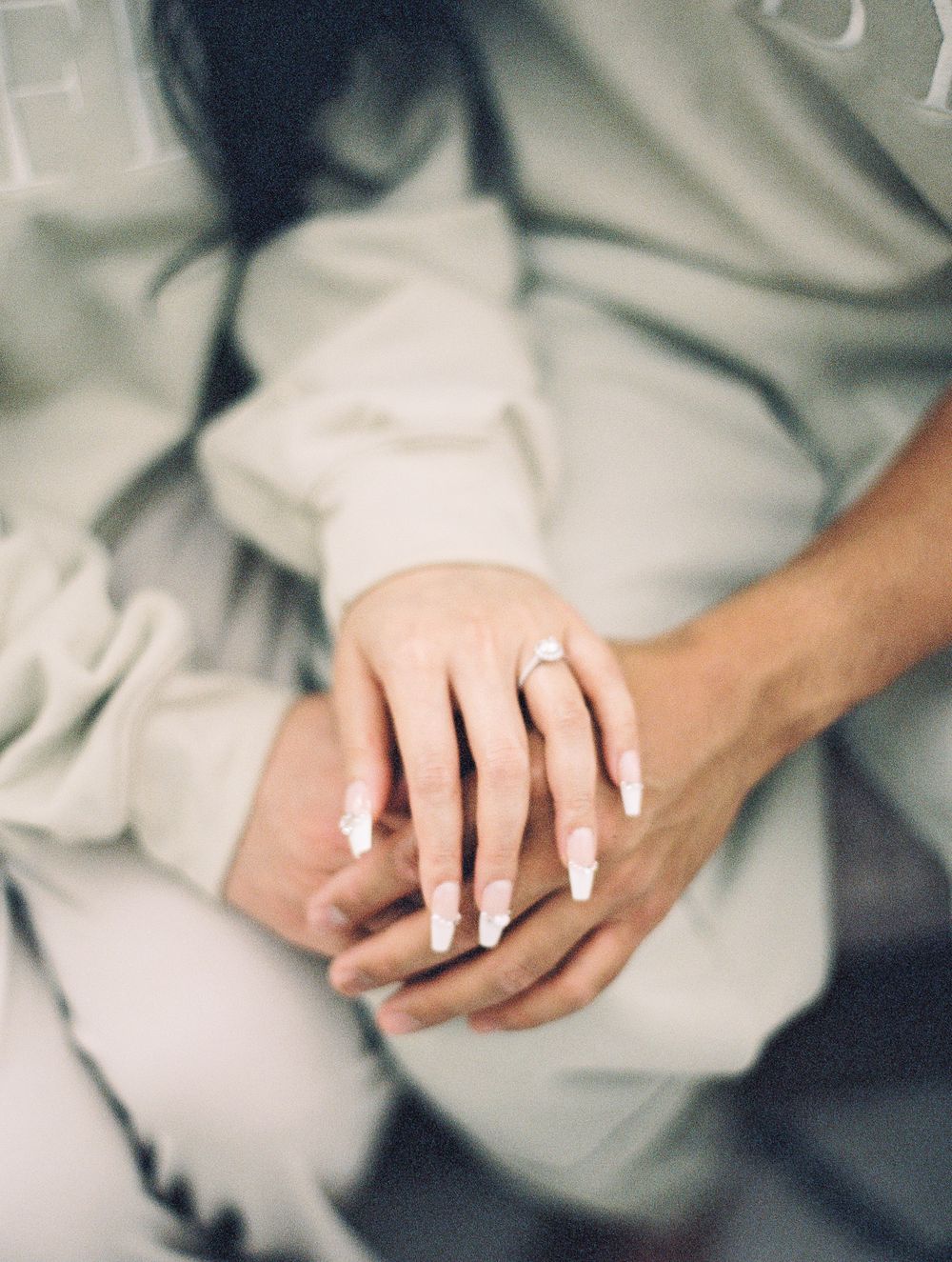 Close up of hands holding together with engagement ring visible on light gray fabric background.