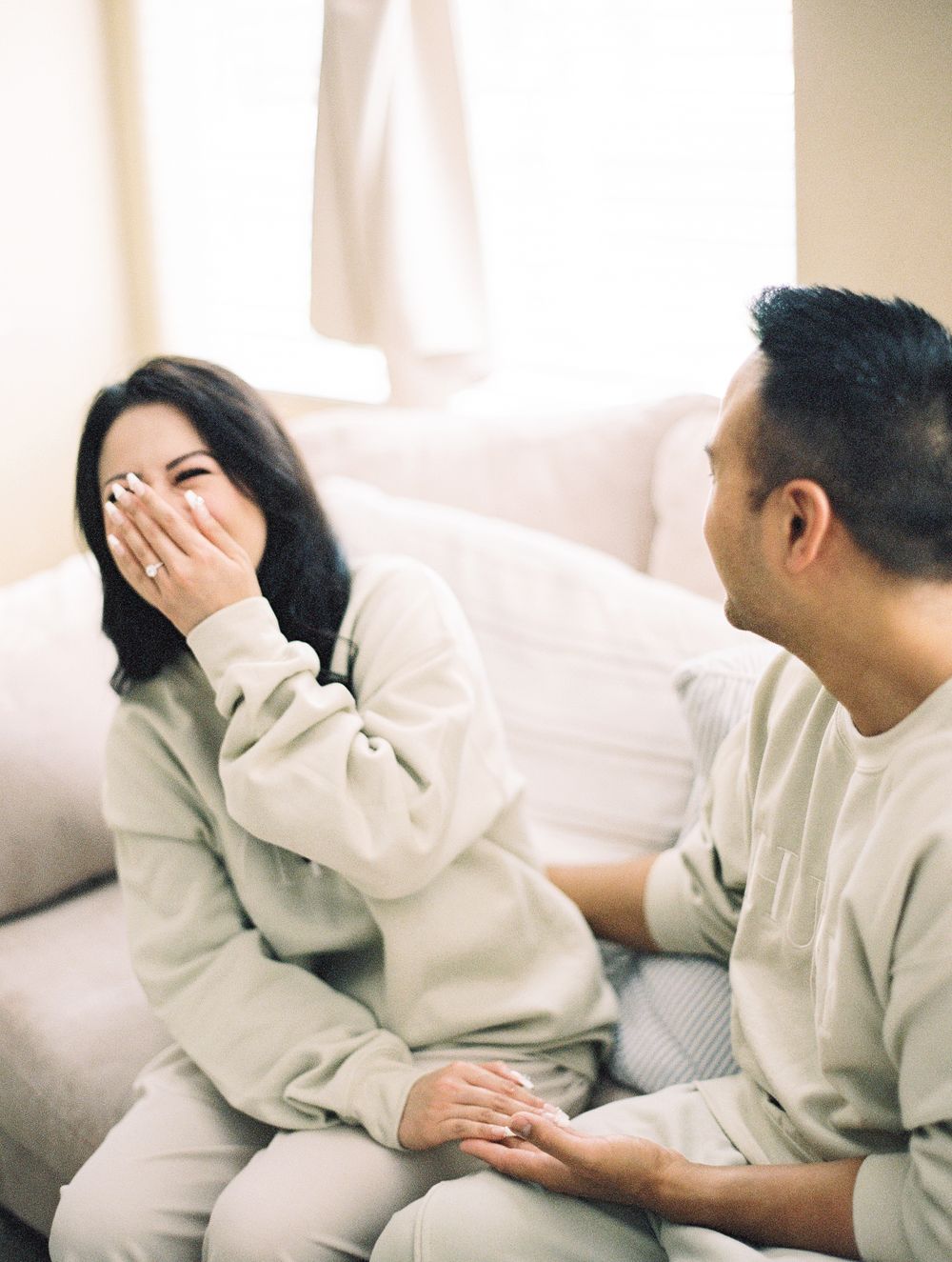 Couple sharing playful moment on couch wearing matching cream colored loungewear.