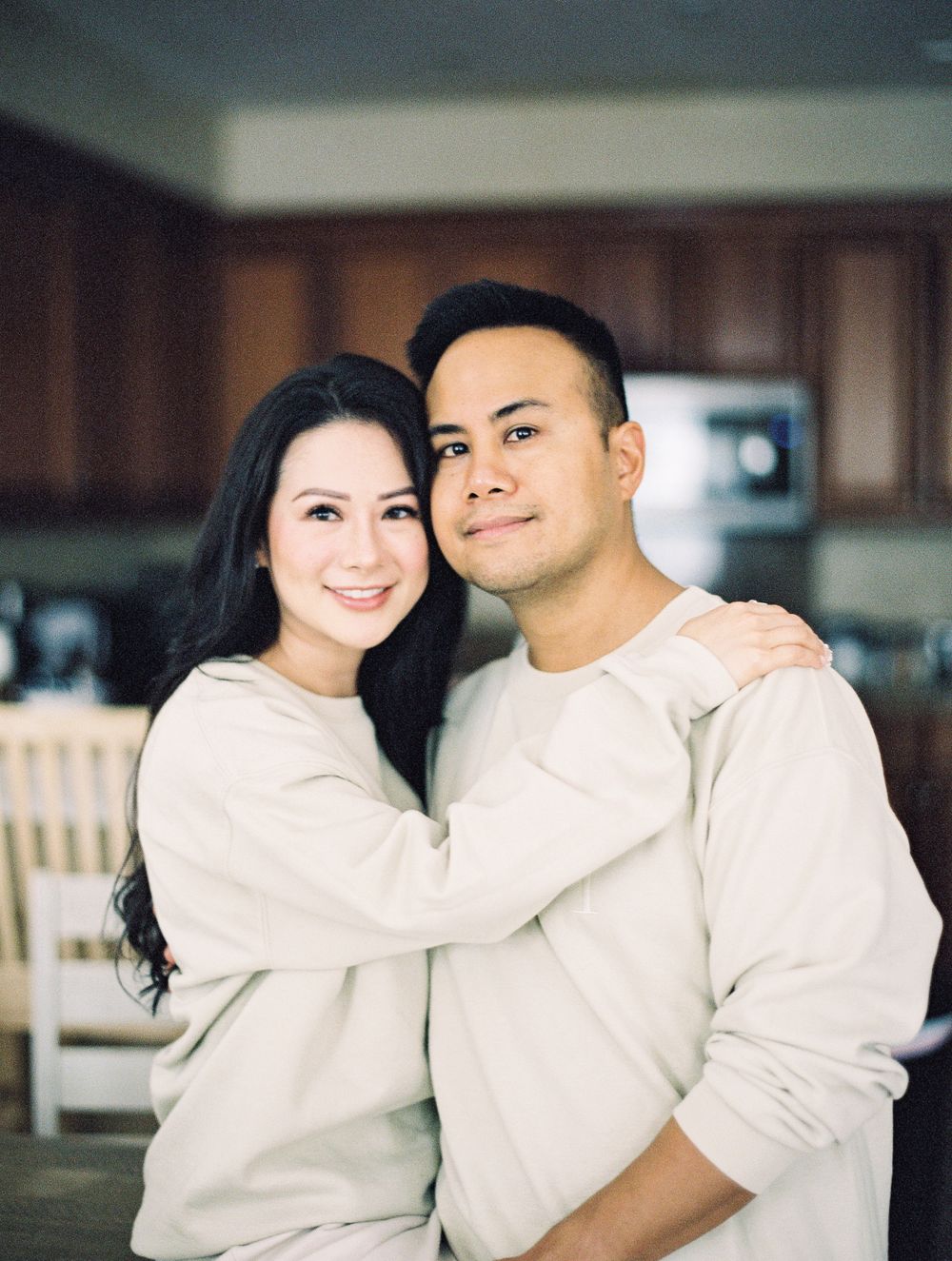 Couple embracing in kitchen wearing matching cream colored sweaters with warm lighting.