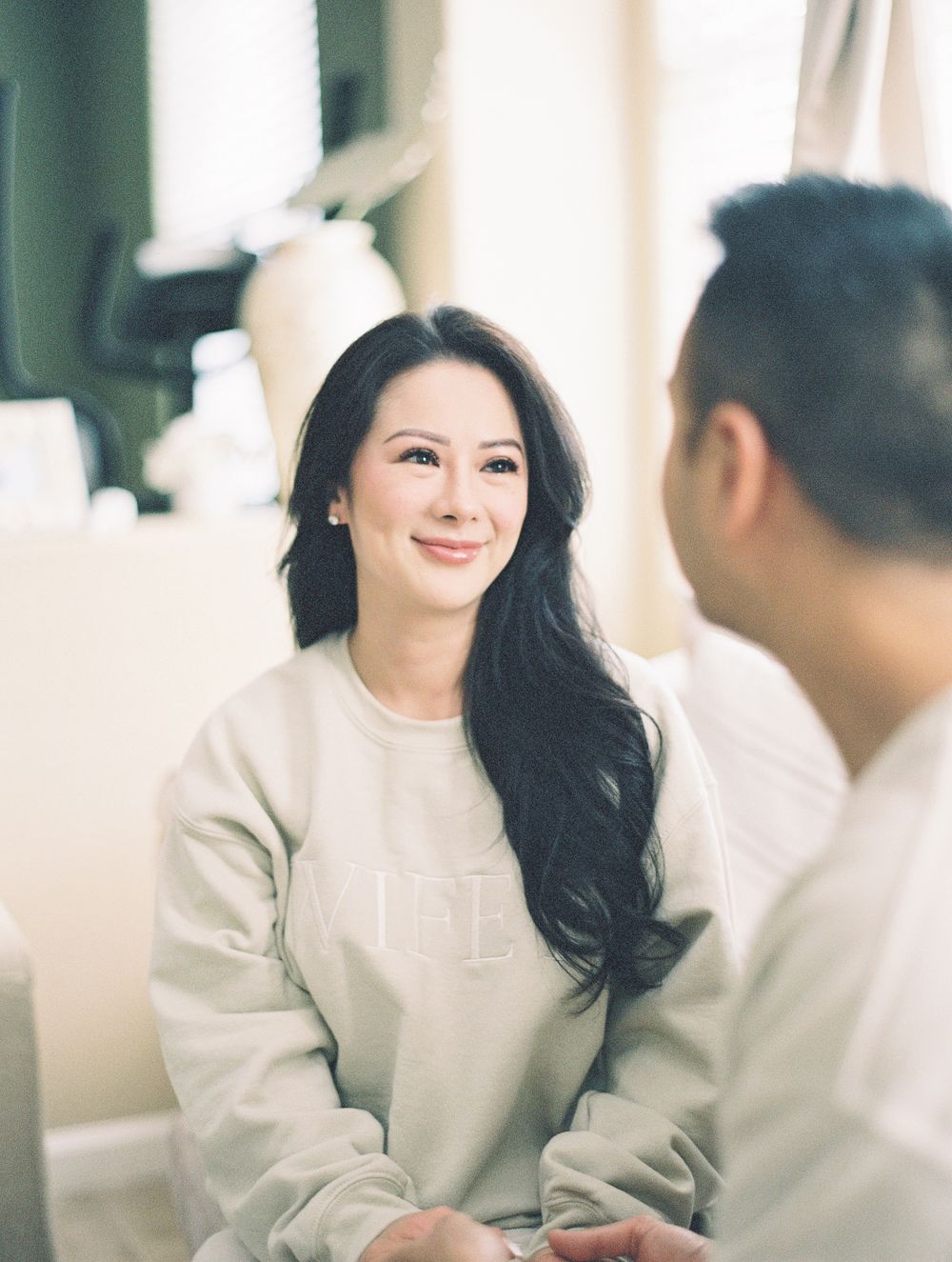 Couple sharing an intimate moment on a couch in cream colored sweaters with soft window lighting.