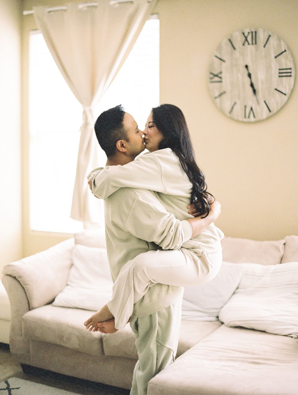 Couple in matching cream outfits sharing romantic moment on light colored couch.