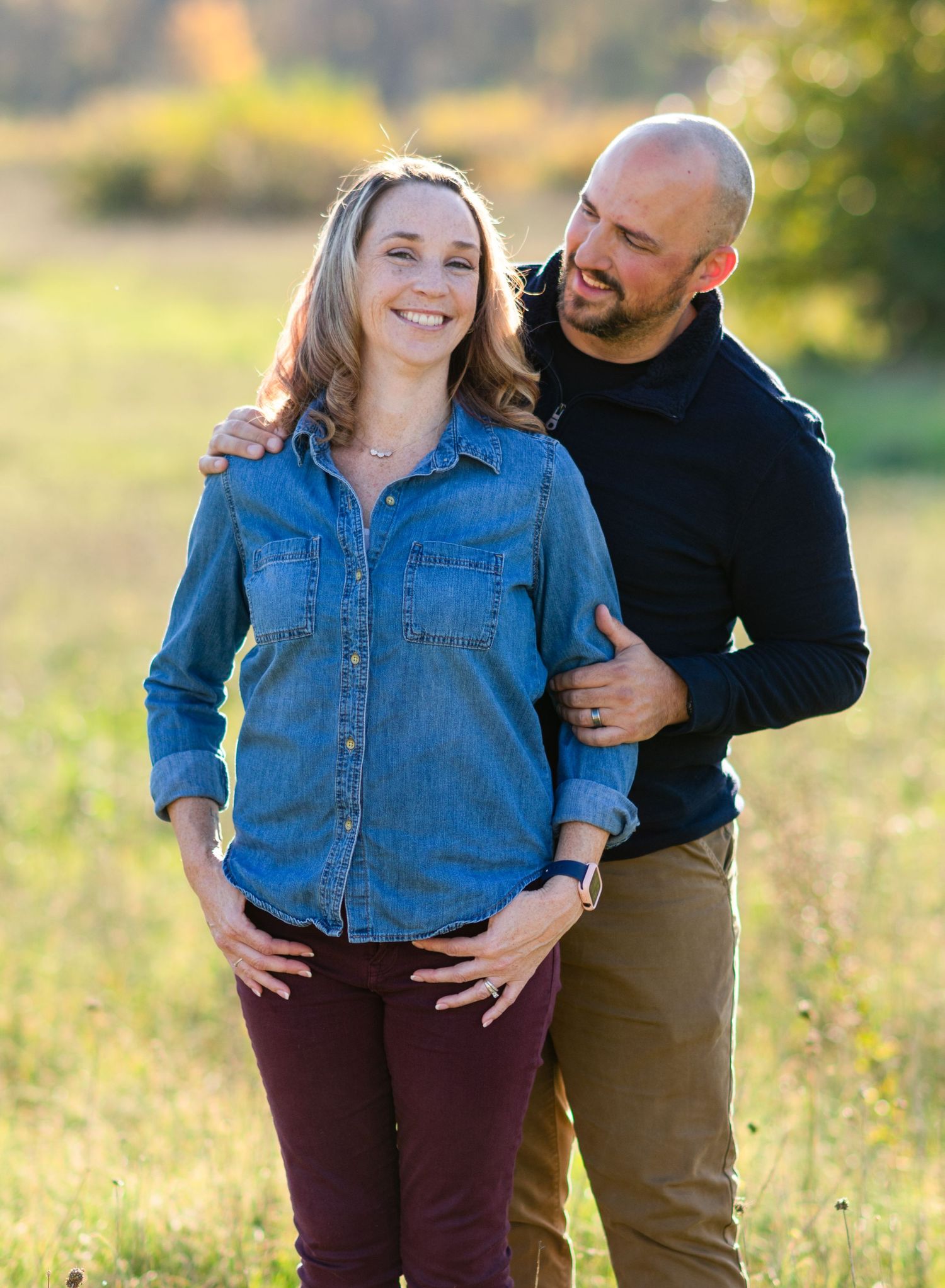 wife looking at camera. husband holding wife and looking at her from behind.