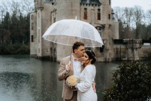 A beautiful bride and groom standing under an umbrella, sharing a romantic moment in front of a majestic castle.