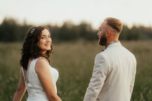 A beautiful couple stands in a field, embracing each other on their special day. They begin their journey together.
