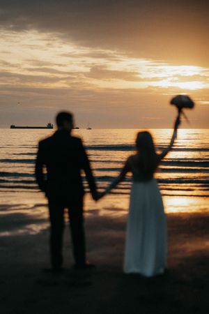 A beautiful moment captured: a bride and groom holding hands on the beach at sunset, creating a romantic silhouette.