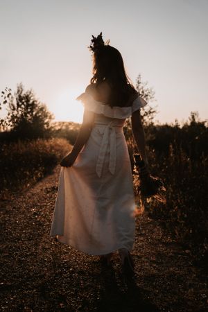 A graceful woman in a white dress strolling along a rustic dirt road, embracing the serenity of nature.