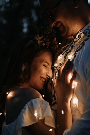 A couple holding hands, standing in a forest during night.