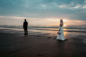 Love in the air as a bride and groom embrace on a beach, with the setting sun casting a golden hue over the horizon.