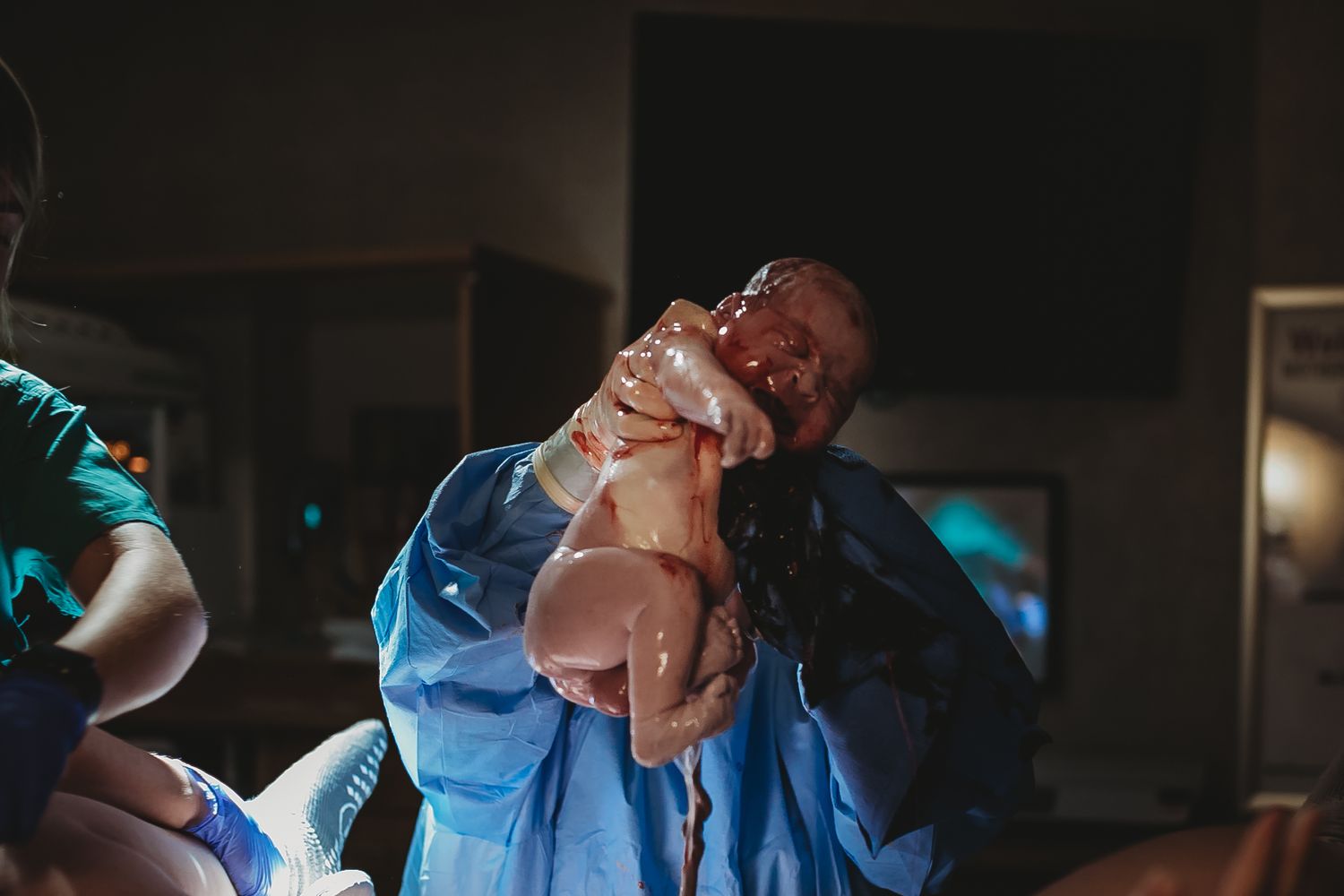 Healthcare provider lifts newborn baby wrapped in blue medical cloth.
