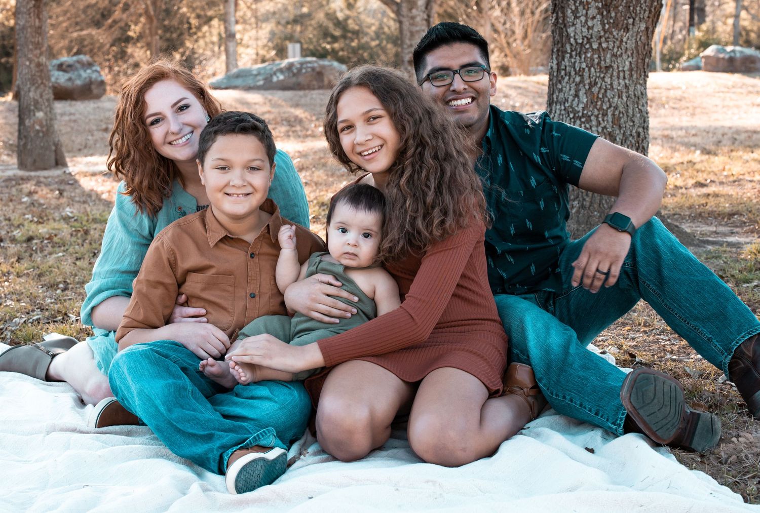Family lounges together on white blanket during outdoor photo session.