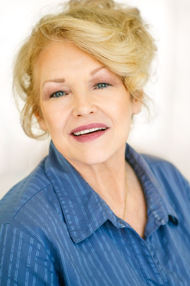 Professional headshot in blue striped shirt with blonde updo against light background.