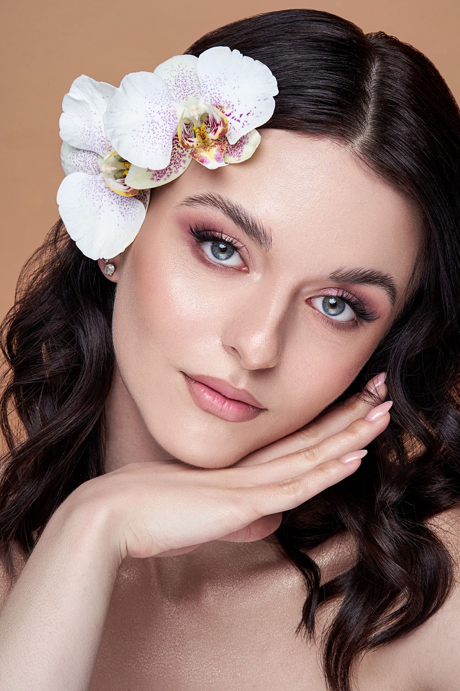 Beauty portrait with glamorous makeup and white orchid flower adorning dark wavy hair in romantic style.