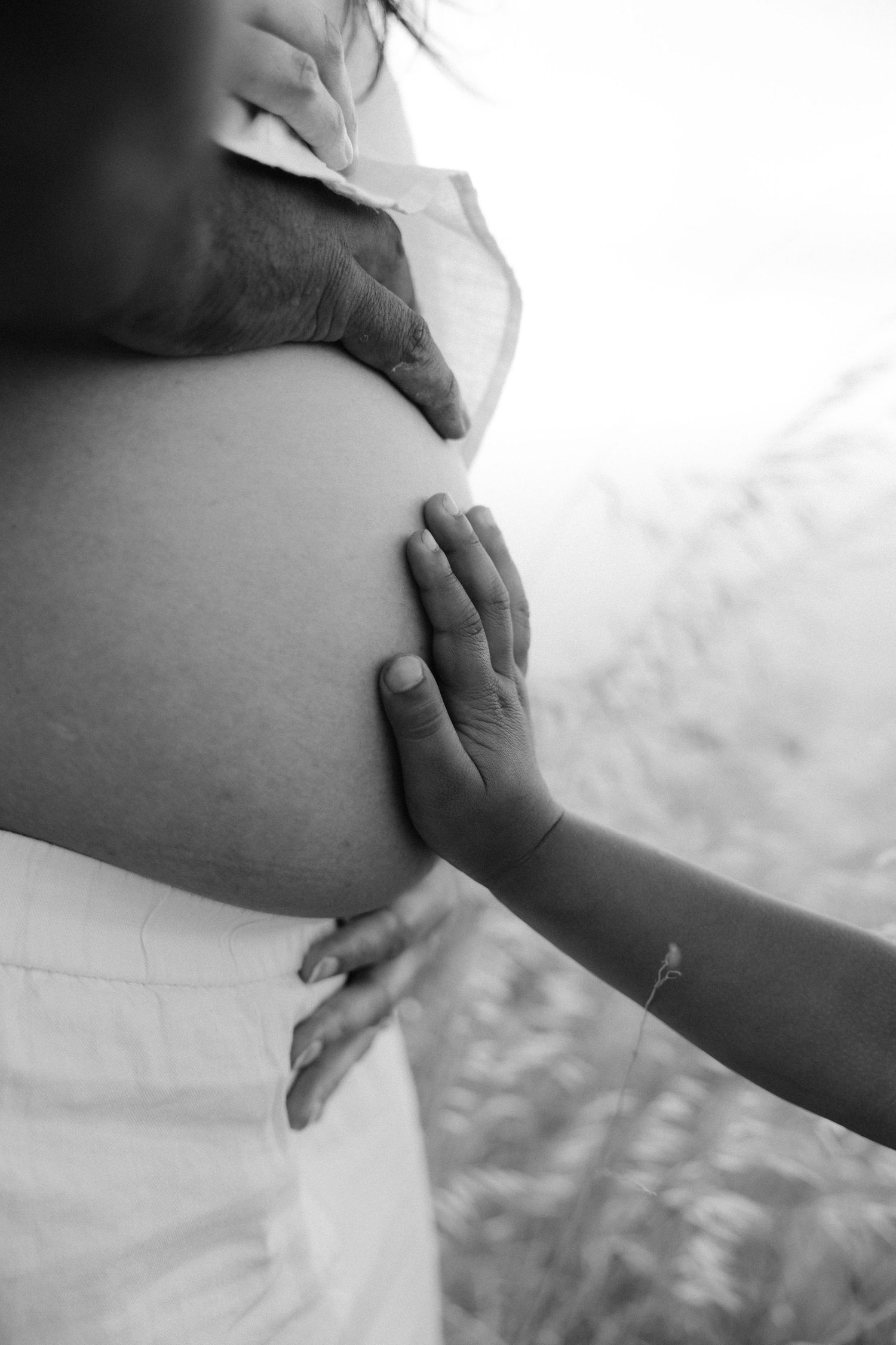 Black and white photo of small child's hand touching pregnant belly.