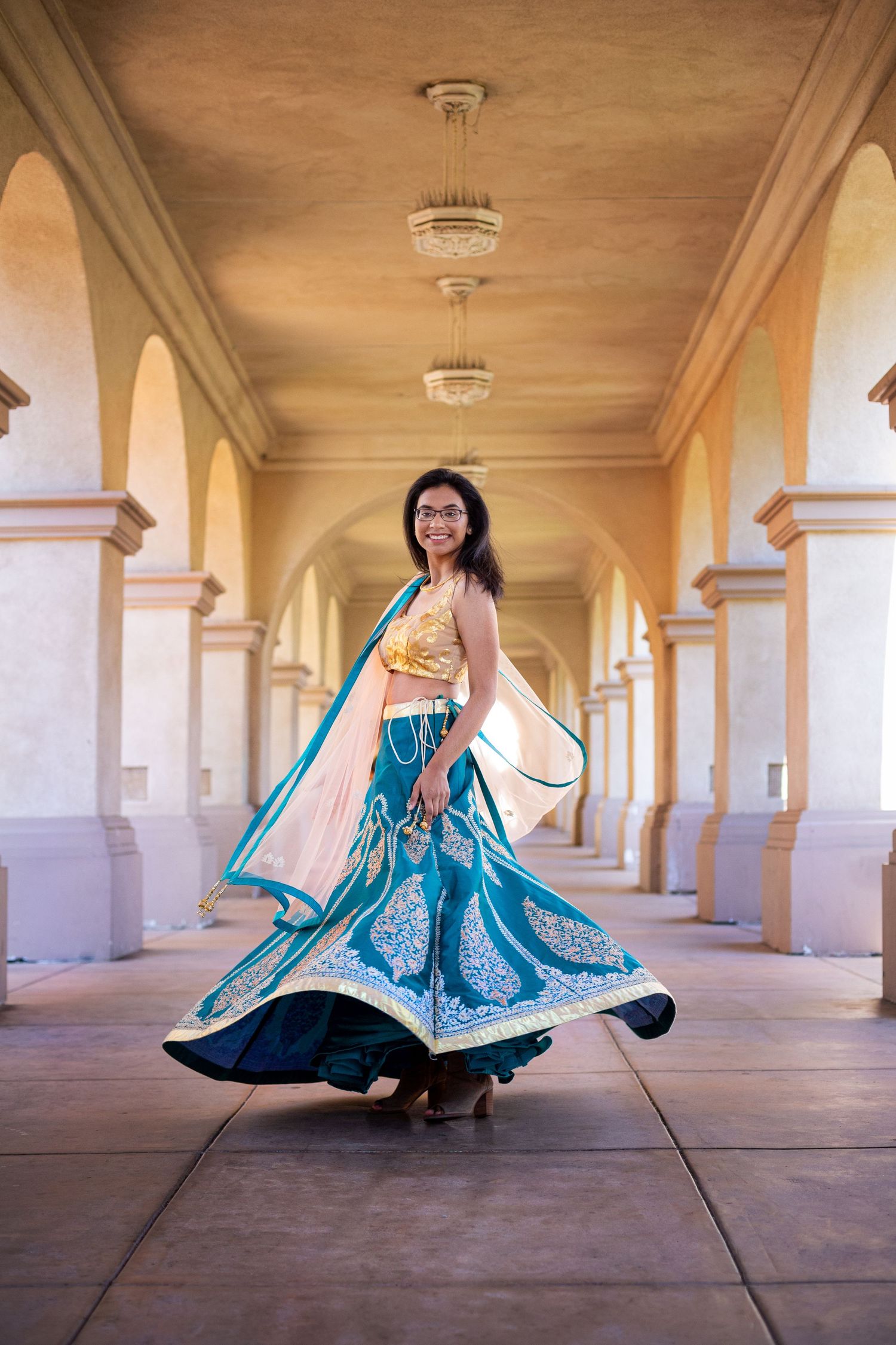 A person twirls in a vibrant blue and turquoise traditional dress beneath an ornate columned archway.