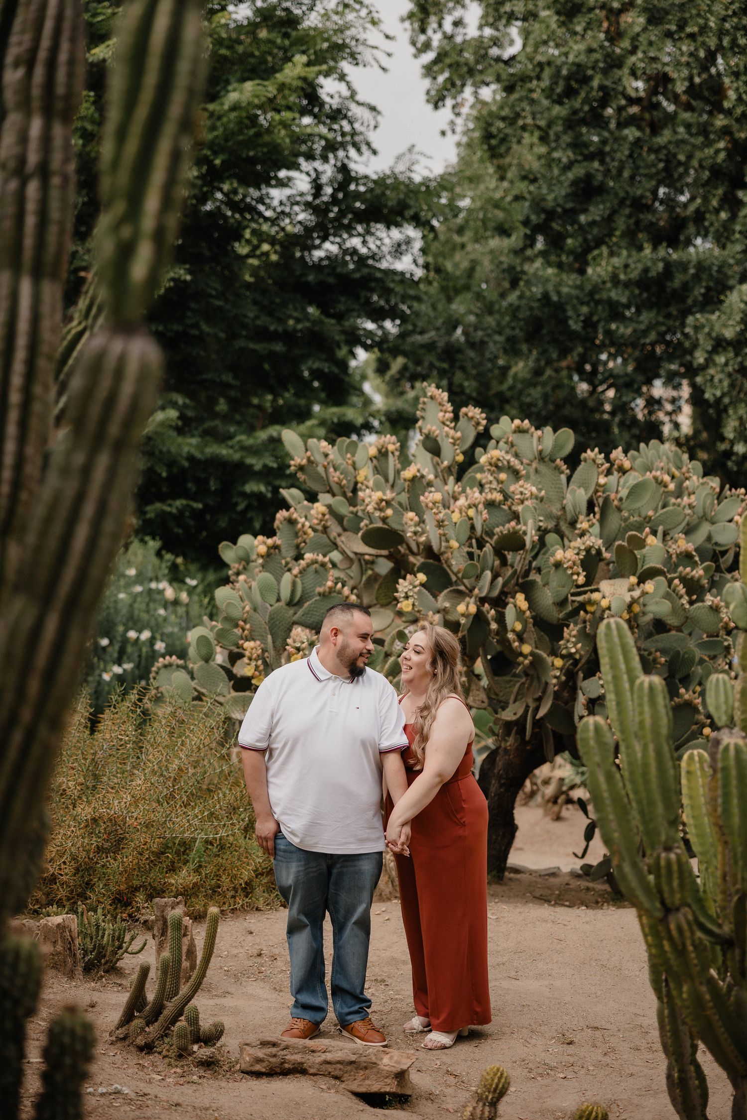 A couple shares an intimate moment together in a desert garden surrounded by towering cactus plants.