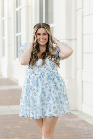 Someone wearing a flowy light blue floral dress poses in front of a bright white column background.