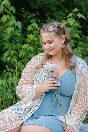 A gentle outdoor photoshoot showing a floral lace cardigan over a blue top amid green foliage.