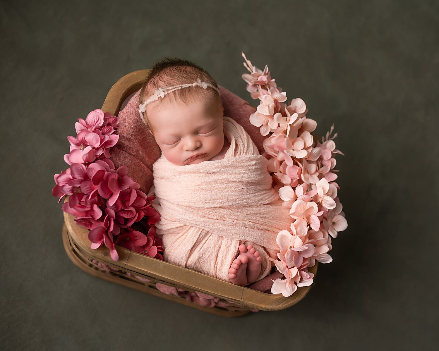 Newborn baby girl wrapped in pink with flowers in heart basket.