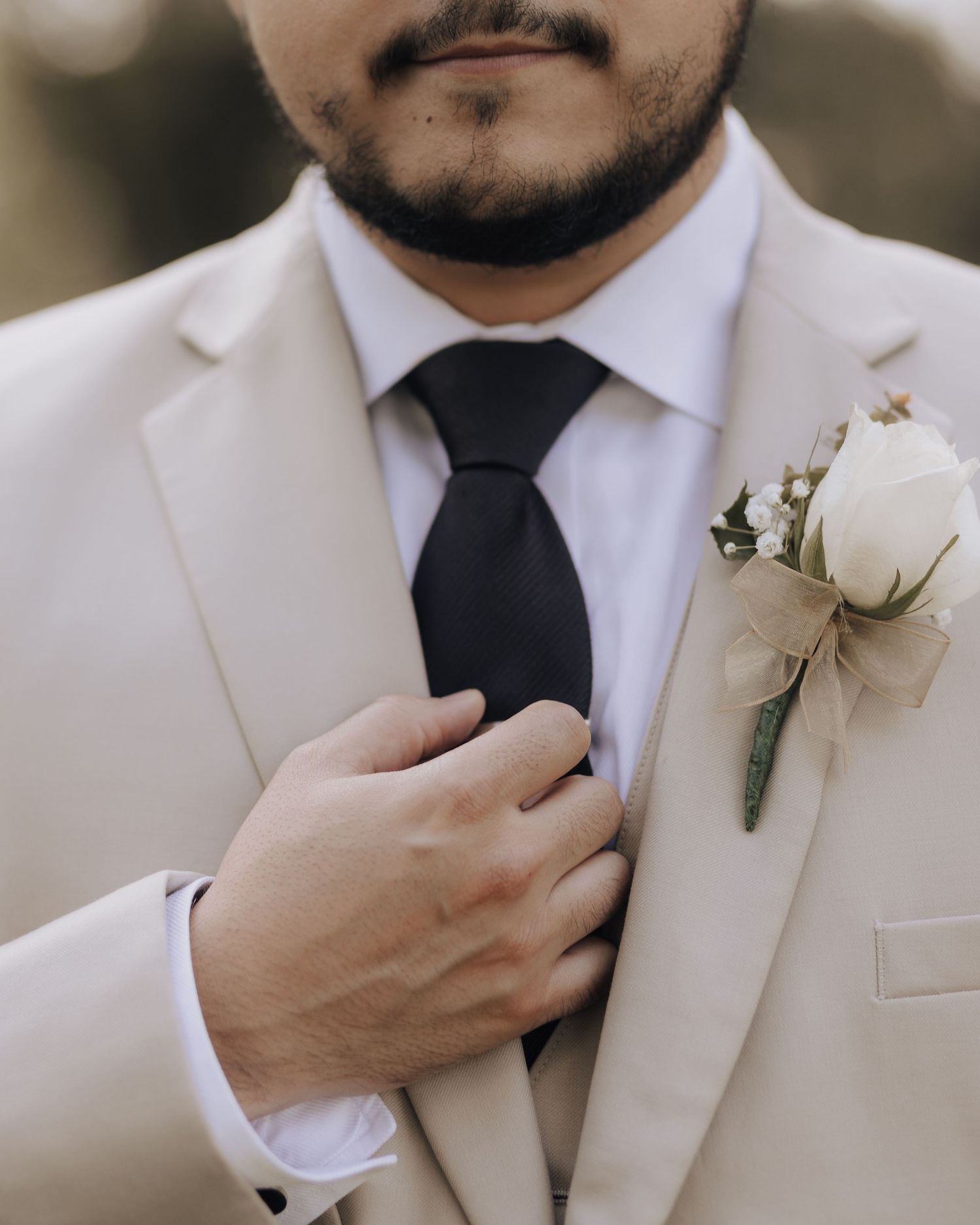 Close-up of a cream suit jacket with black tie and white rose boutonniere.