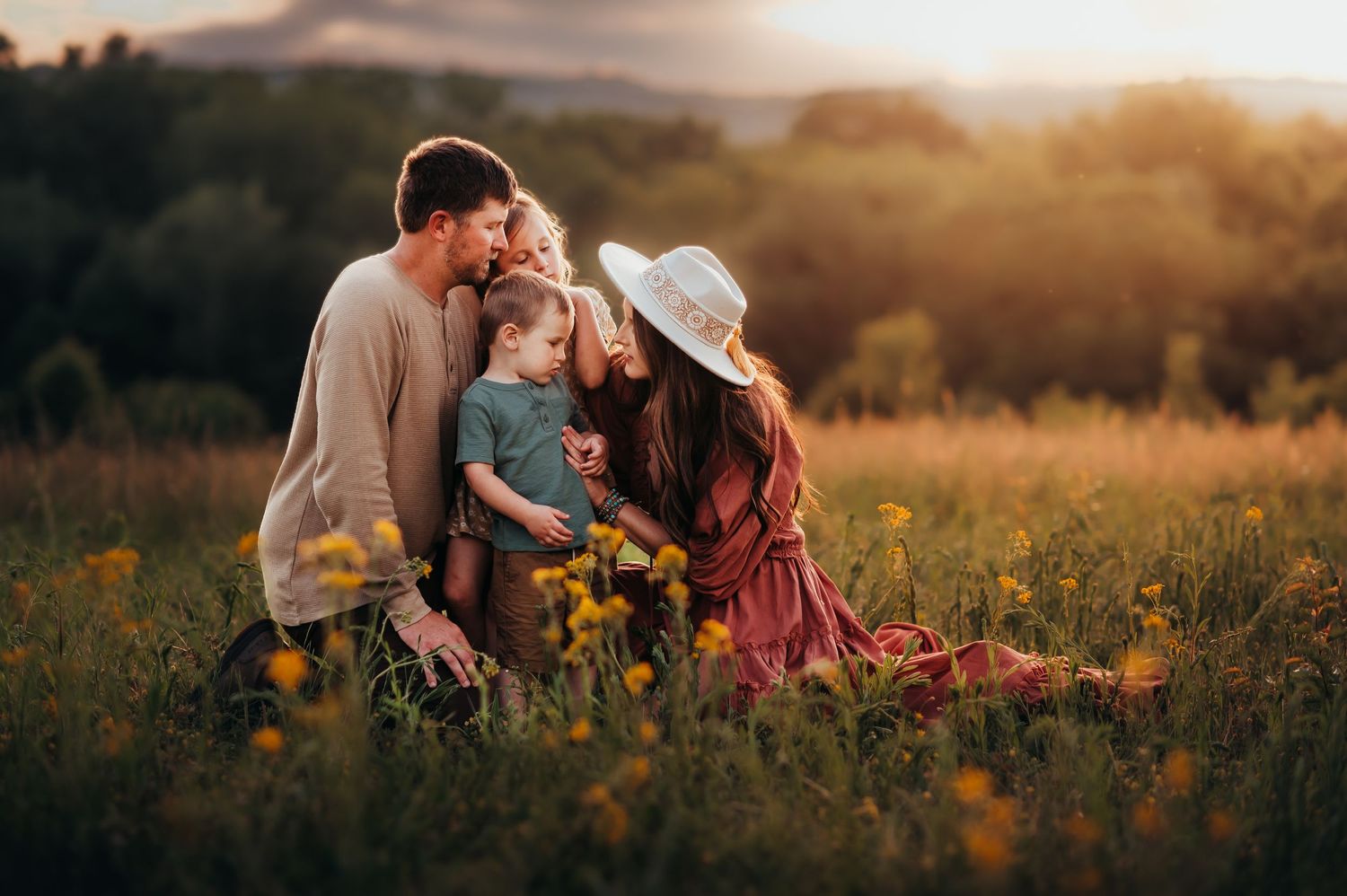 Family of 4 kneels in a whileflower field at sunset with the Chattanooga mountains behind them for family photo session