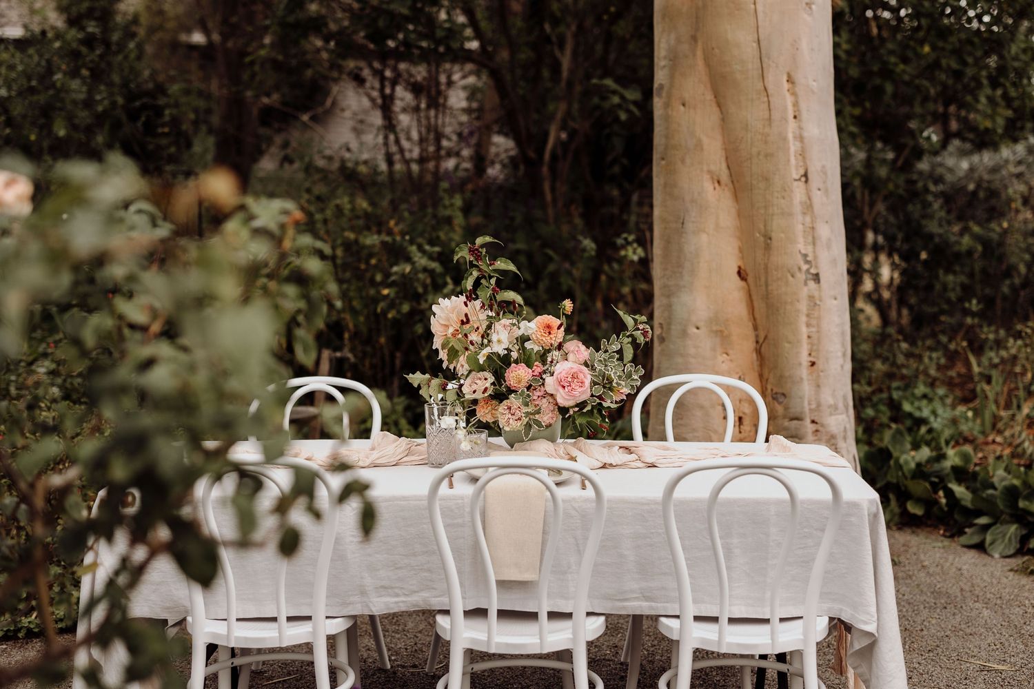Elegant outdoor table setting with white chairs and floral centerpiece.