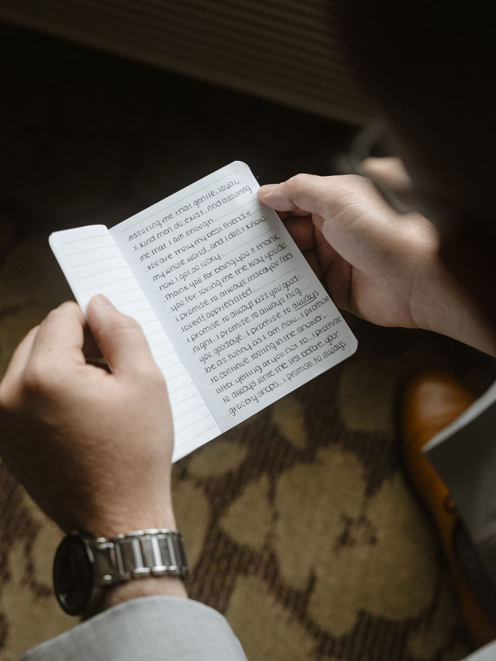 Hands holding a small book with text, wearing a silver watch.