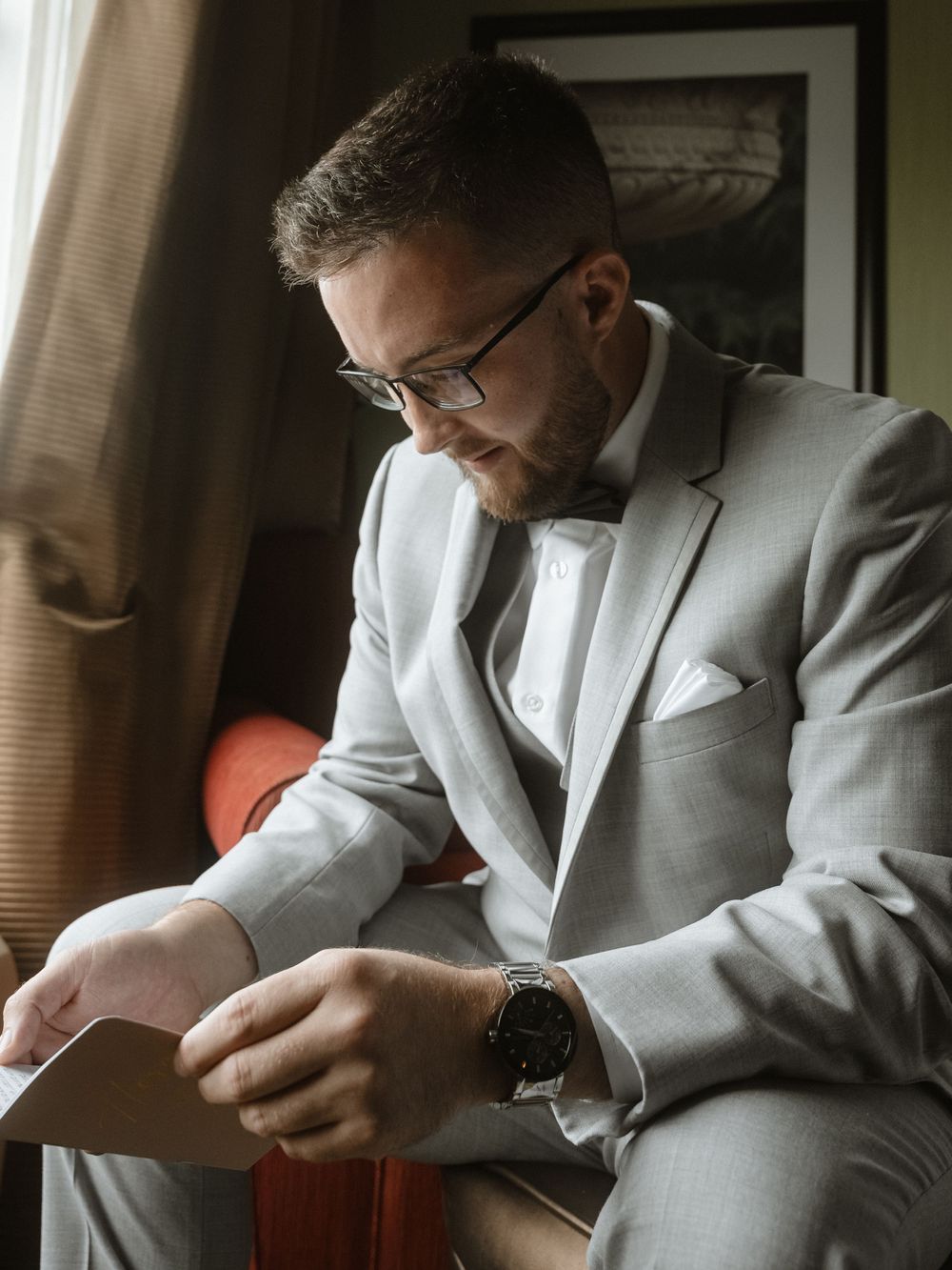 Person in light grey suit and glasses reading a card while seated.