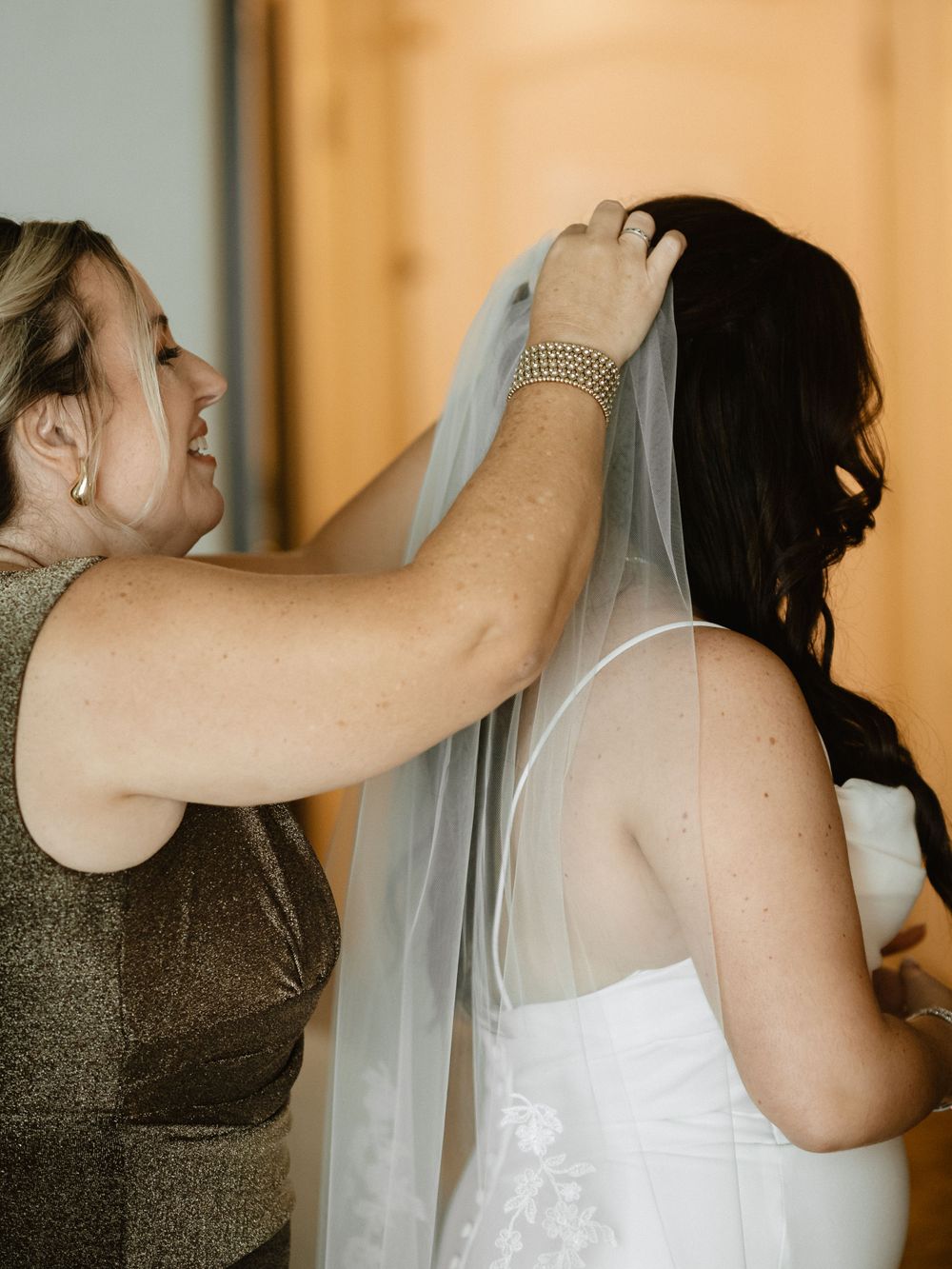 Someone helps adjust a wedding veil during bridal preparations.