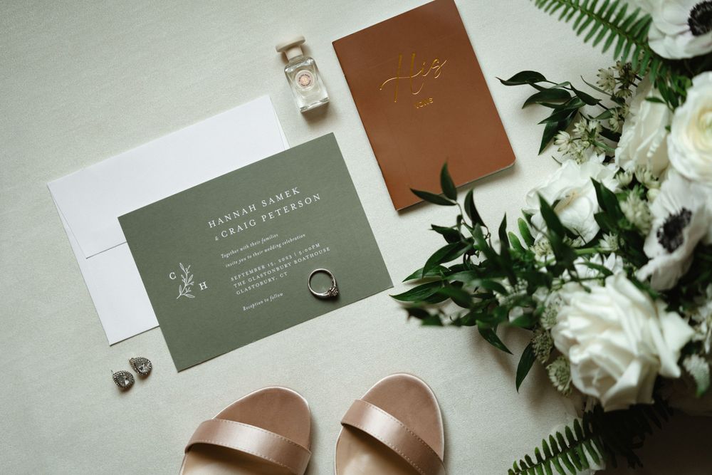 Wedding invitation suite with green envelope, copper details, and white florals.