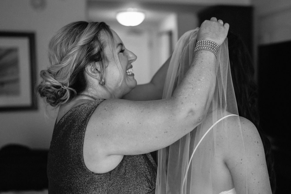 Black and white photo of someone helping to place a wedding veil.
