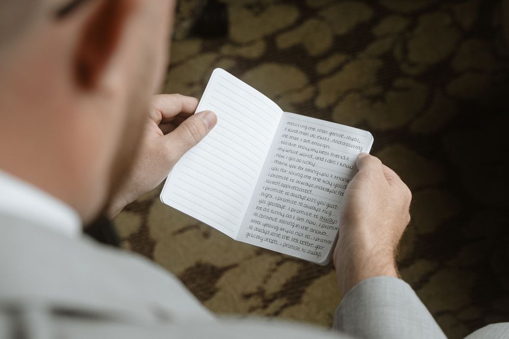 Person reading from a small white book while seated.