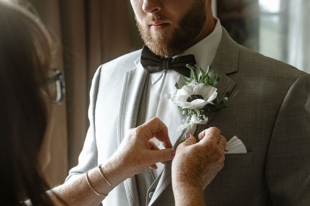 Someone adjusting a white boutonniere on a grey suit lapel.