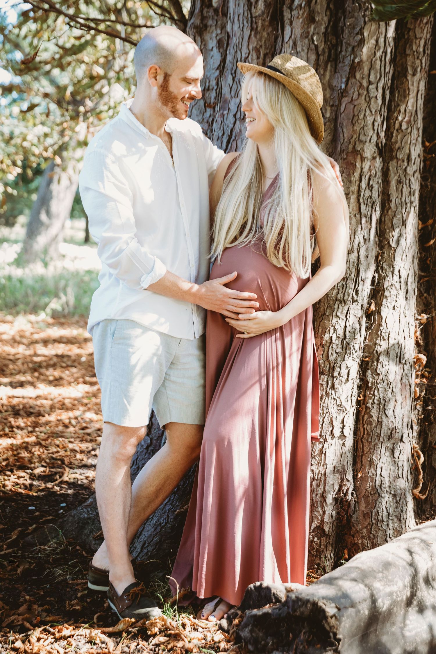 A couple shares an intimate moment during their maternity photoshoot in a wooded setting.