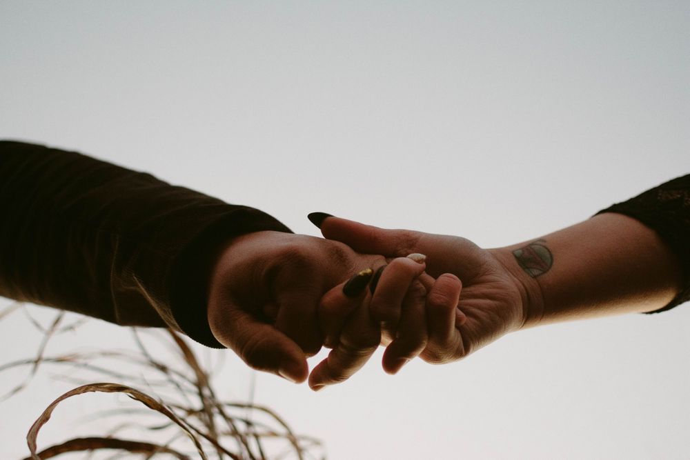 Two hands reach out to touch in a romantic silhouette against a bright sky.