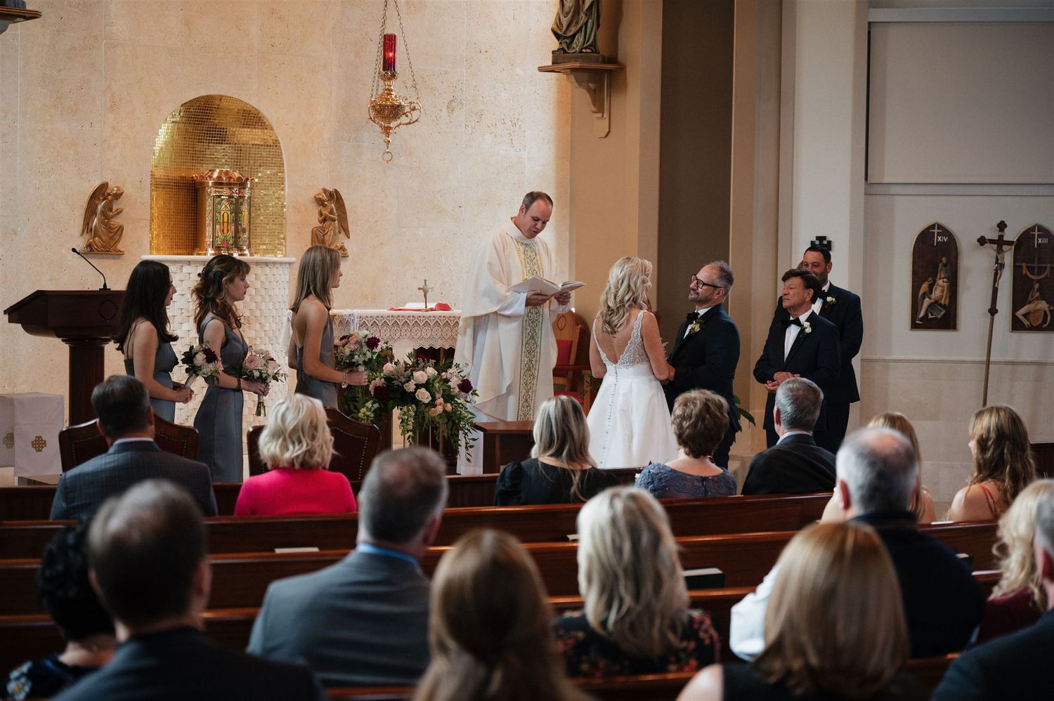 Catholic wedding ceremony taking place at church altar surrounded by religious statues and artwork.