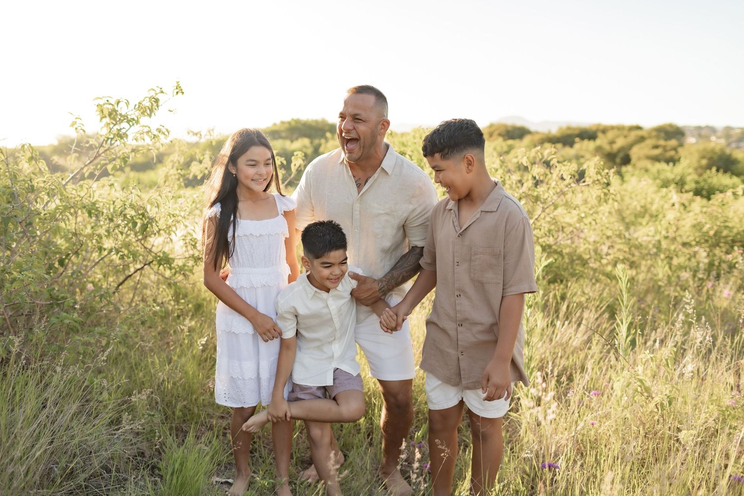 Family of four stands together in a golden field during sunset.
