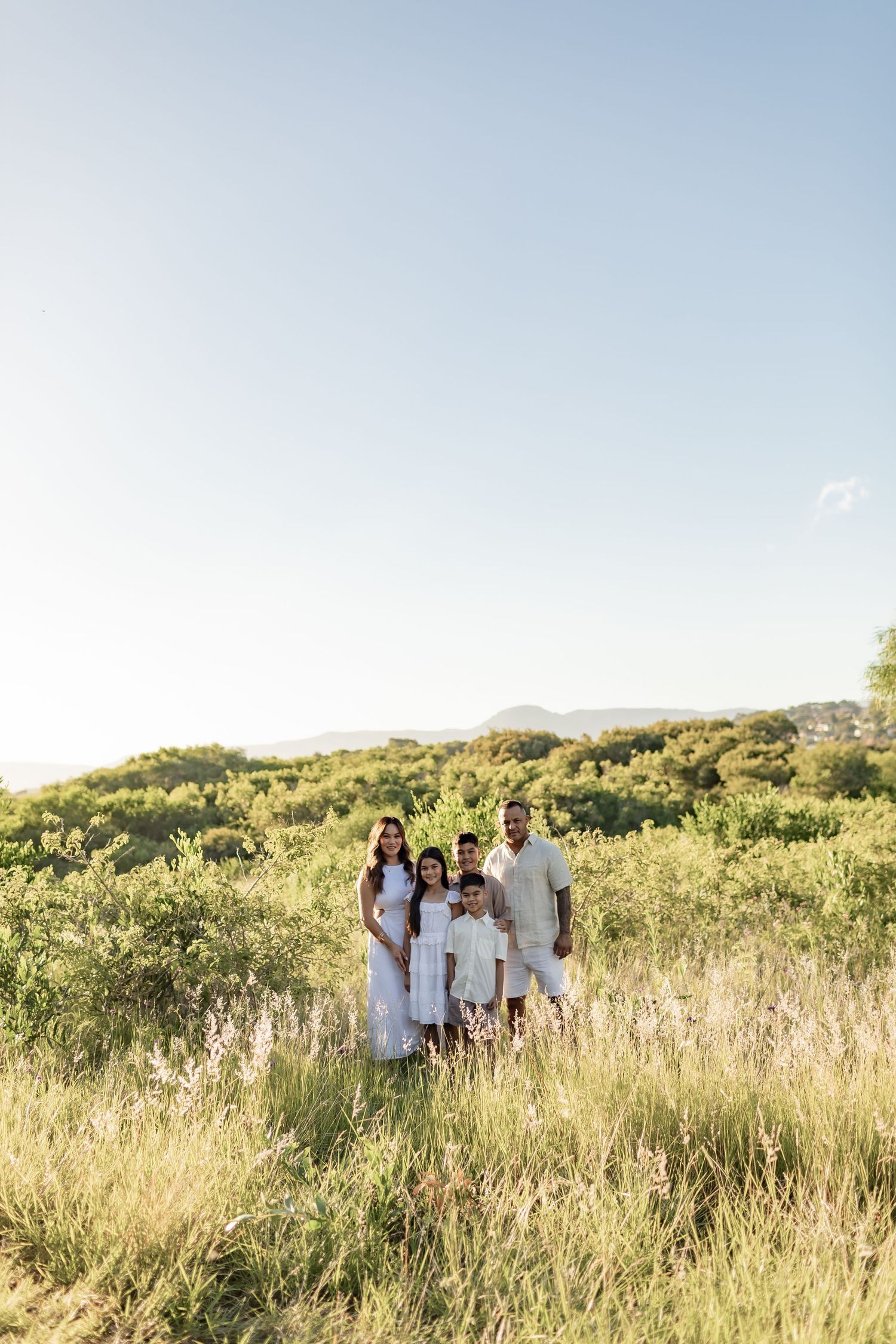 Group photo of people in white clothing standing in tall grass with mountains in background.