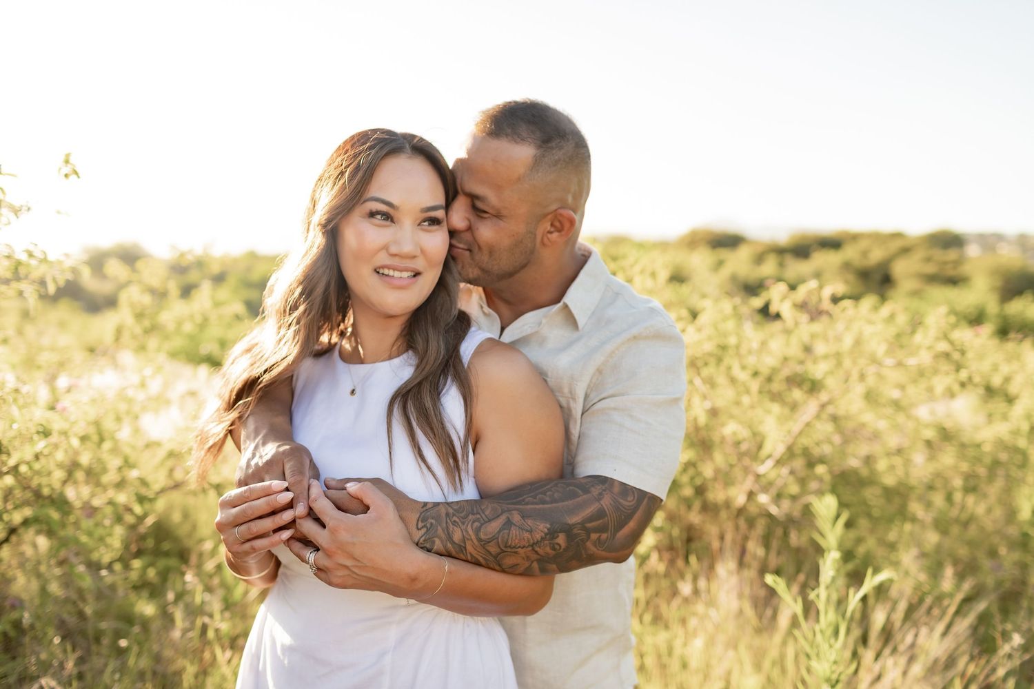 Intimate portrait of couple in white clothing sharing tender moment in sunlit field.