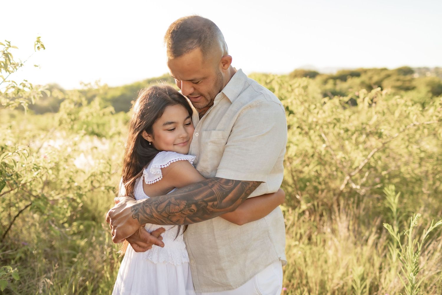Parent and child share a tender embrace amidst tall grass in a golden field.