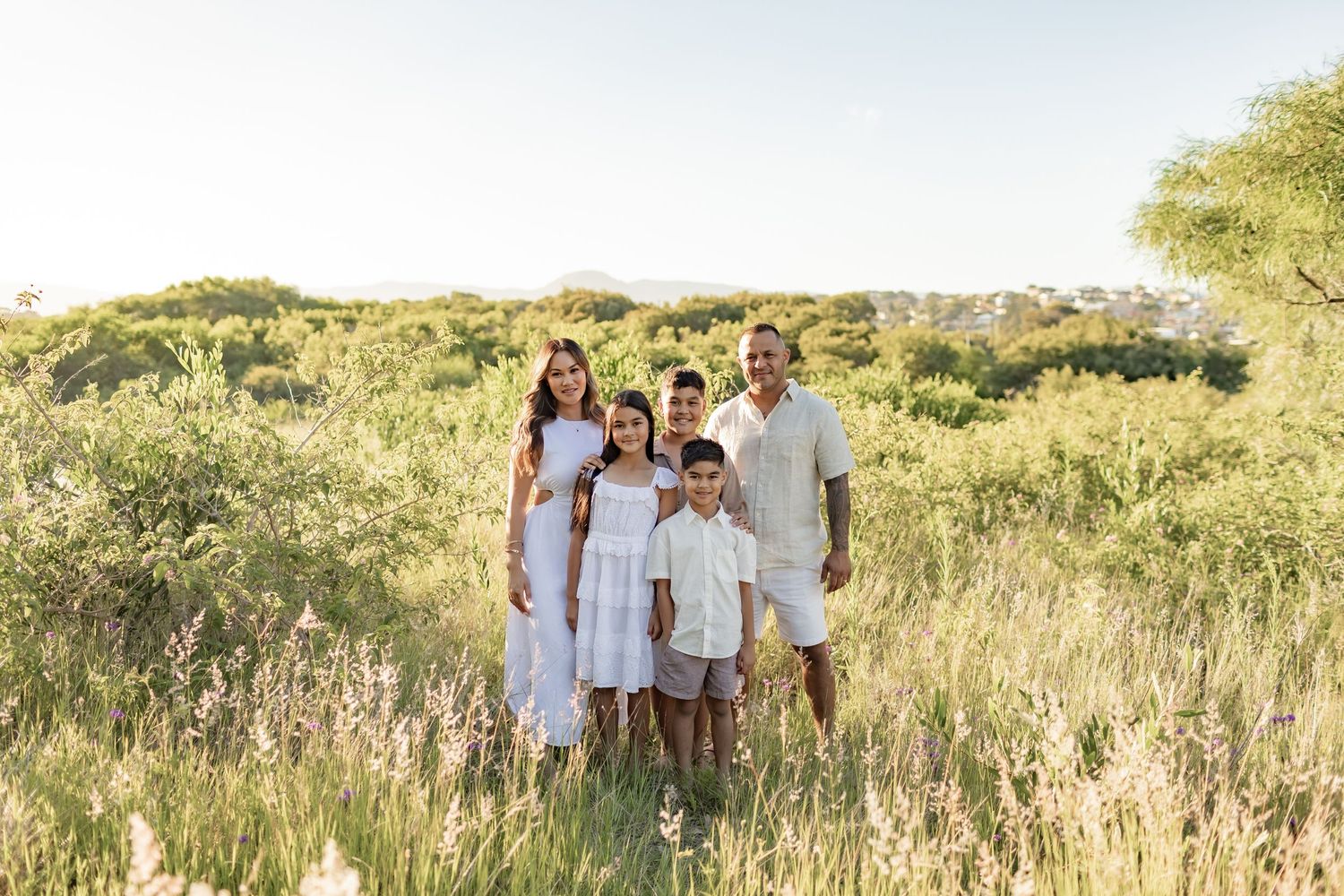 Family wearing white outfits standing together in a grassy field at sunset.