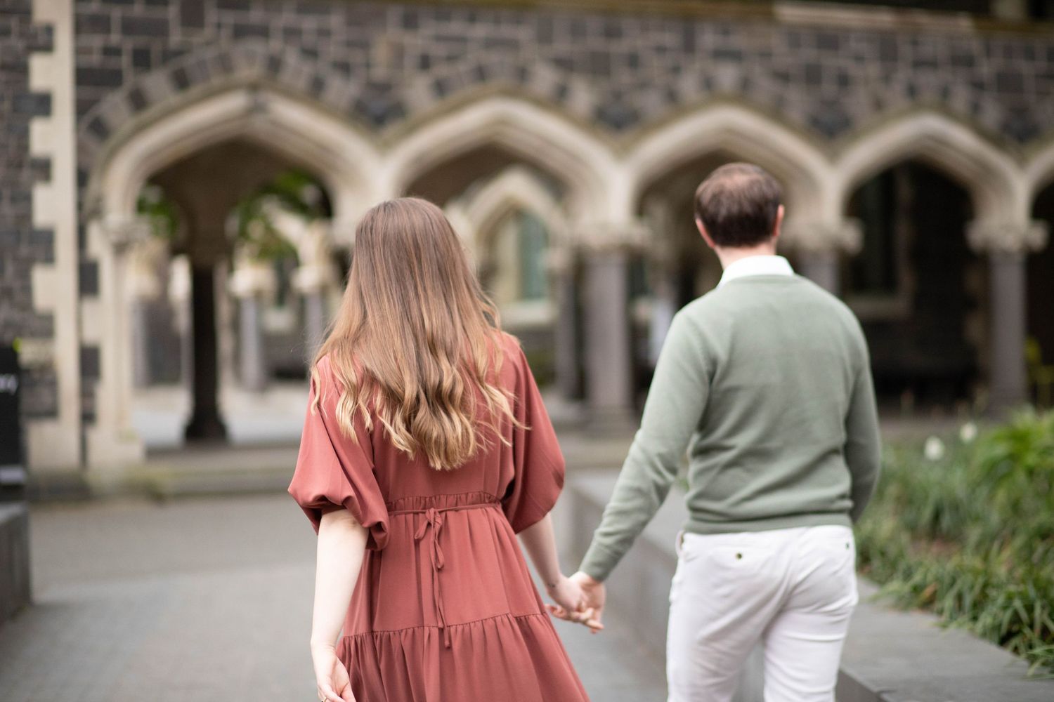 landscape close up image of a couple holding hands walking together towards a arched hallway