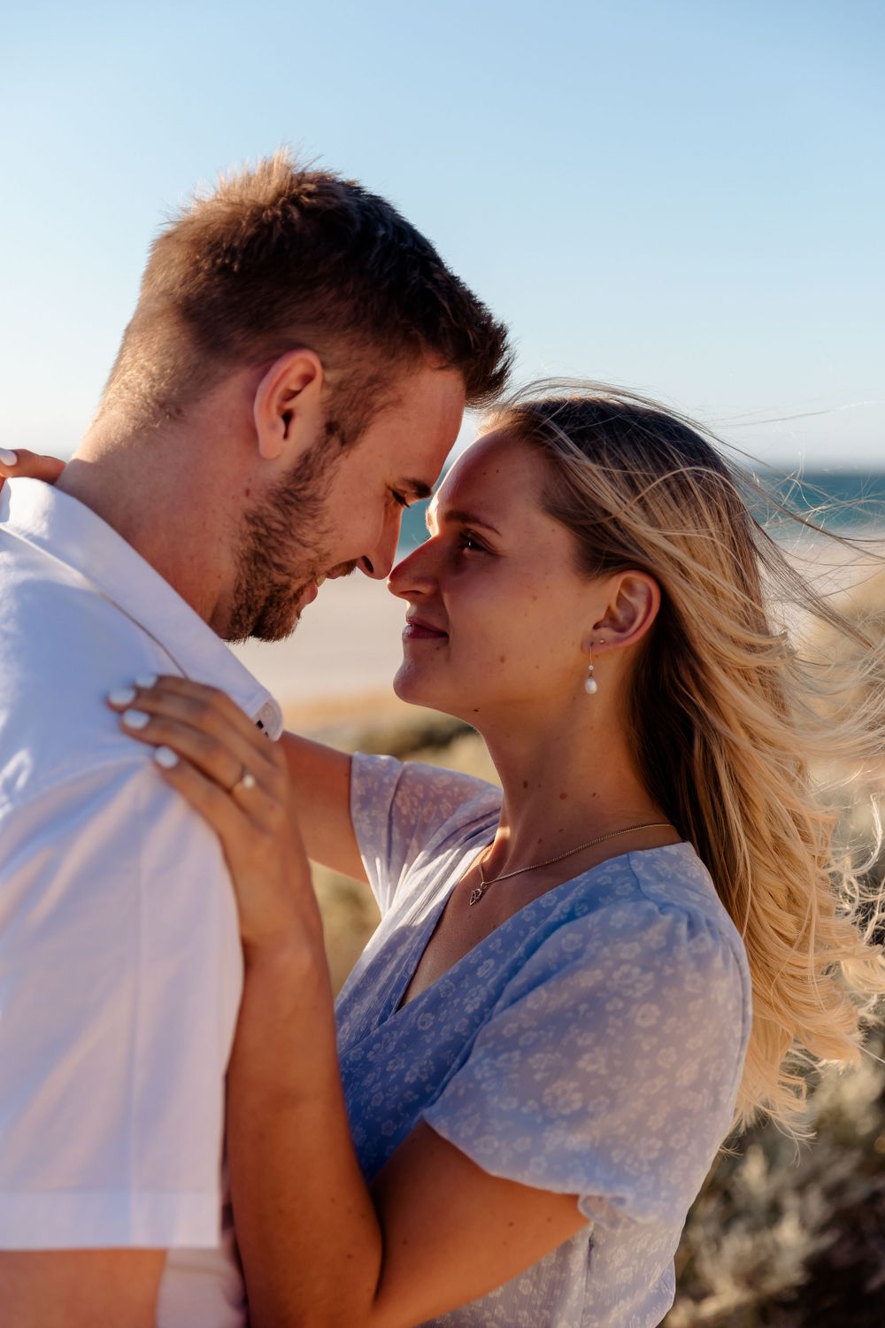 Romantic couple sharing an intimate moment against a bright blue sky background.