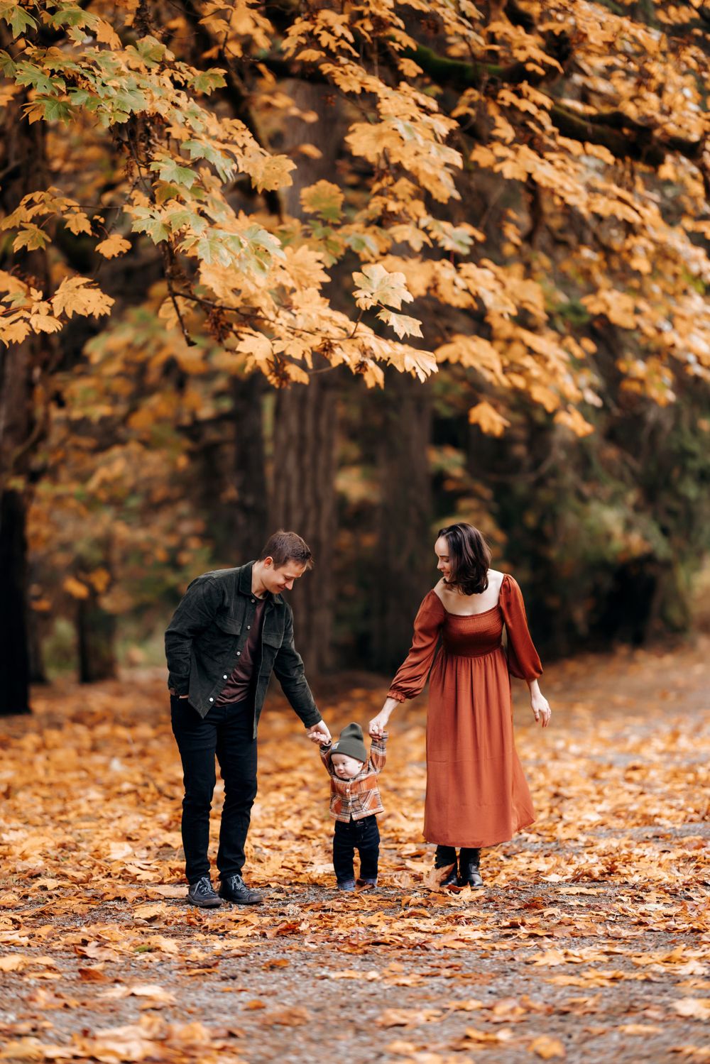 Family walking together on path covered in golden autumn leaves.