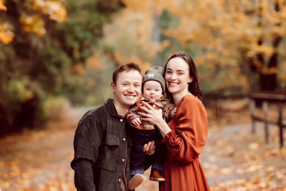 Family portrait in autumn setting with golden leaves and natural lighting.