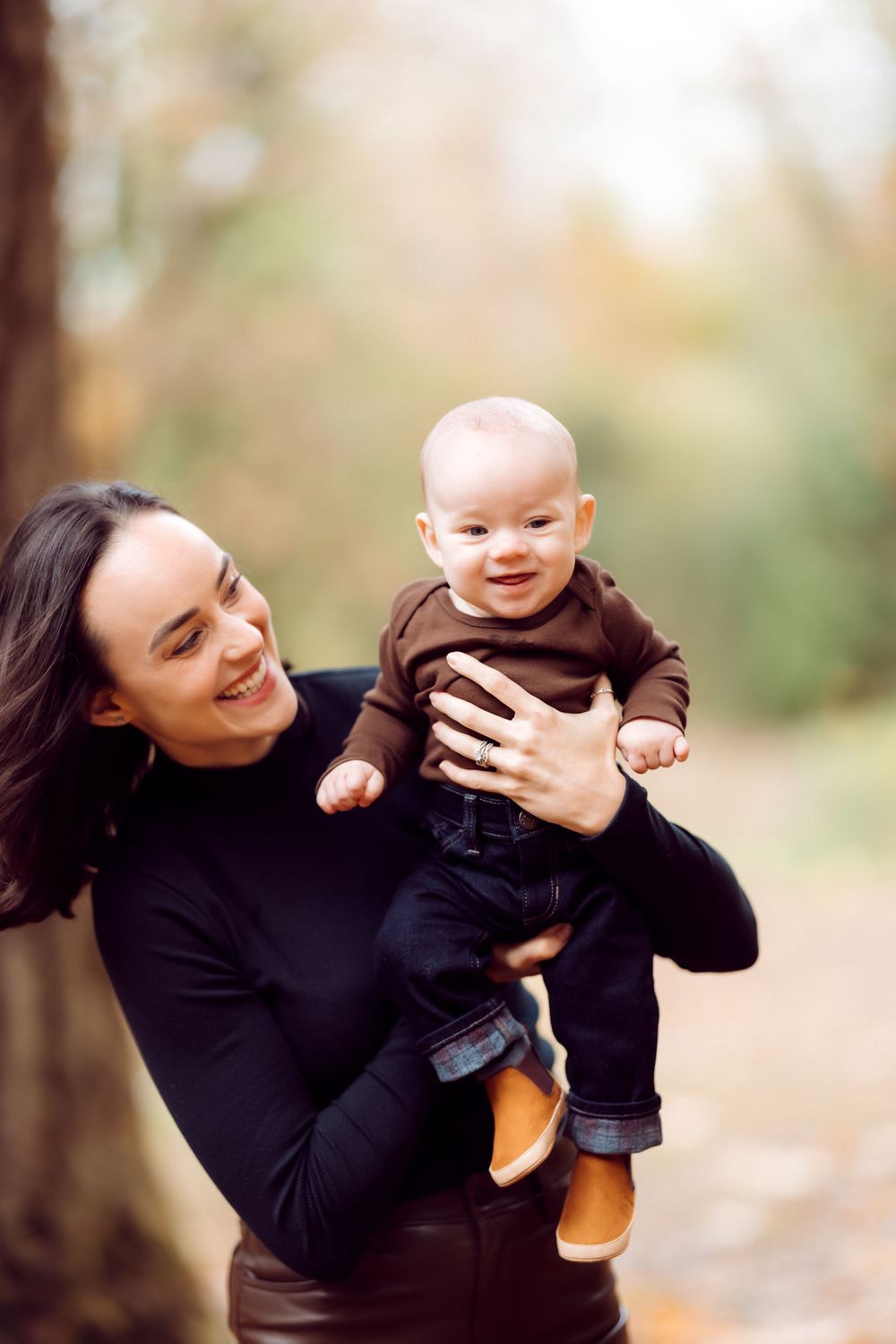 A parent and baby share a joyful moment outdoors in casual attire.