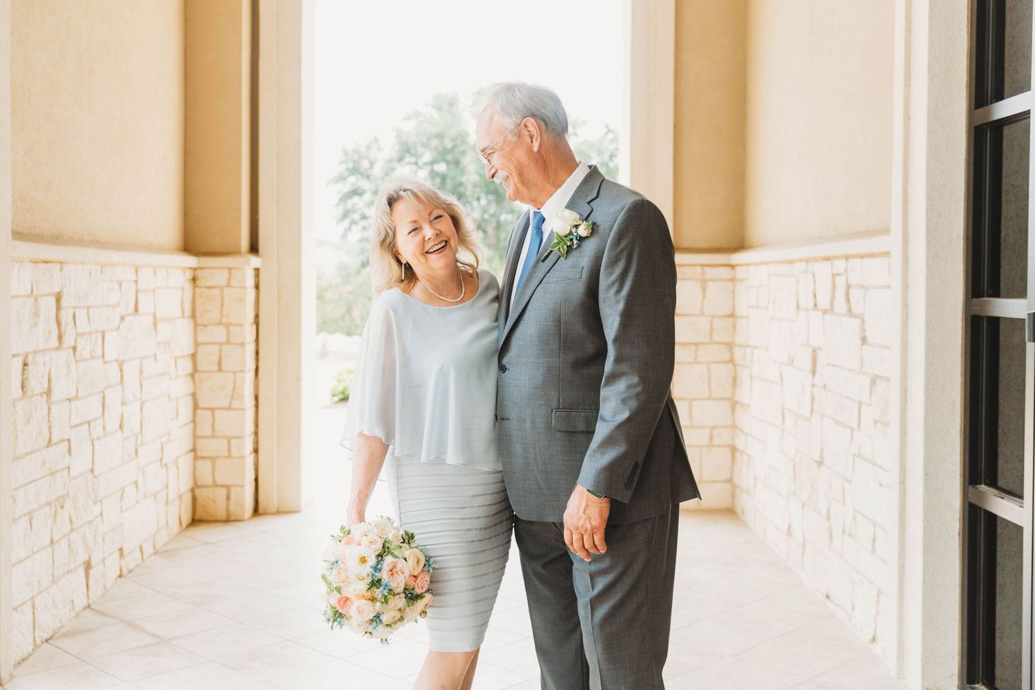 Couple walking hand in hand down a bright stone hallway with romantic natural lighting.
